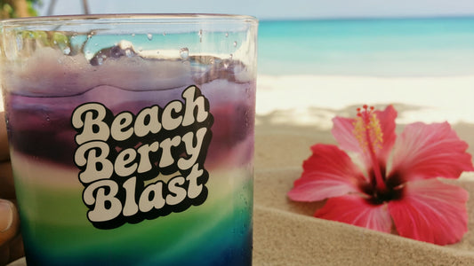 Beach Berry Blast recipe. Hand holding a purple and green drink on a sunny beach.