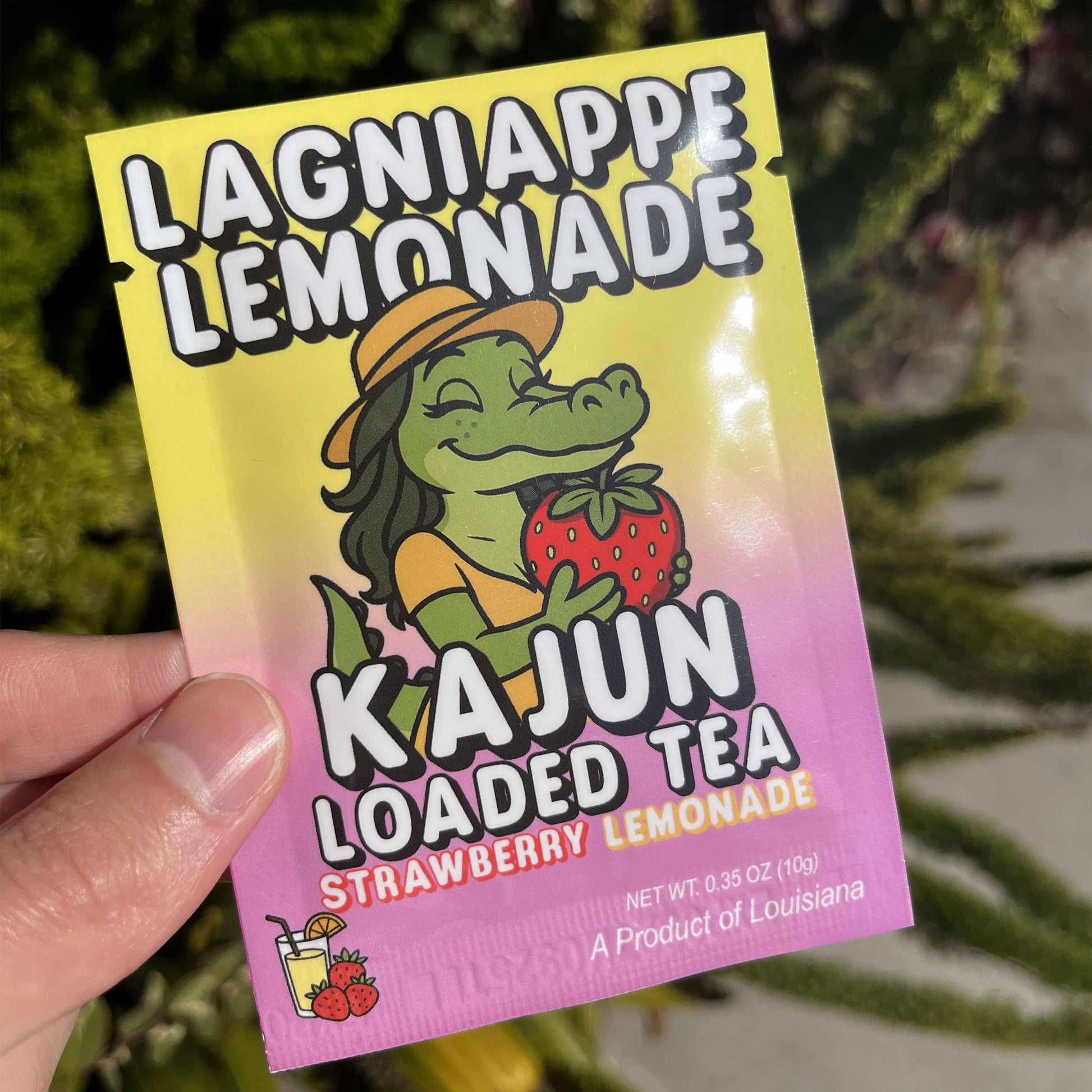 Lagniappe Lemonade Kajun Loaded Tea packaging held by a hand with a blurred green background
